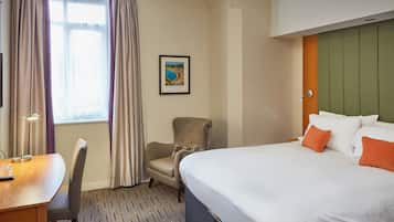 Habitación de hotel con cama, escritorio, silla y ventana con cortinas.