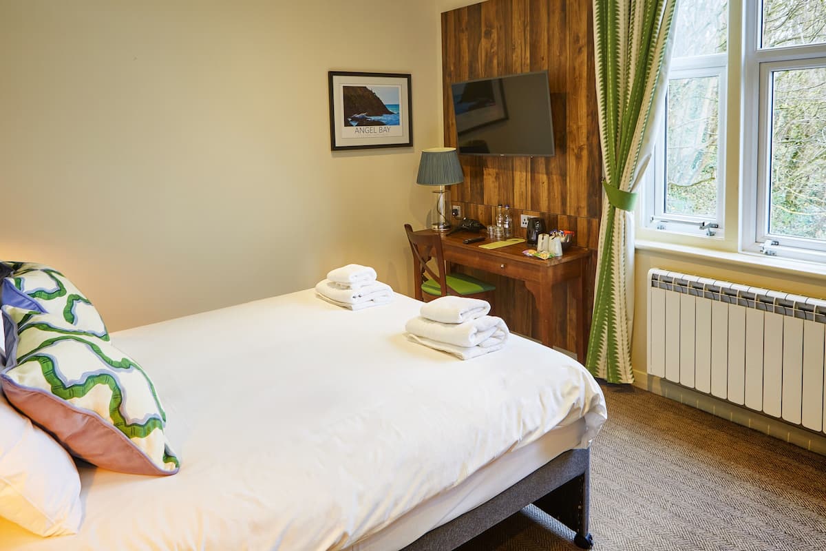 Une chambre d’hôtel équipée d’un lit, d’un bureau, d’une chaise, d’une télévision et d’une fenêtre avec des rideaux.