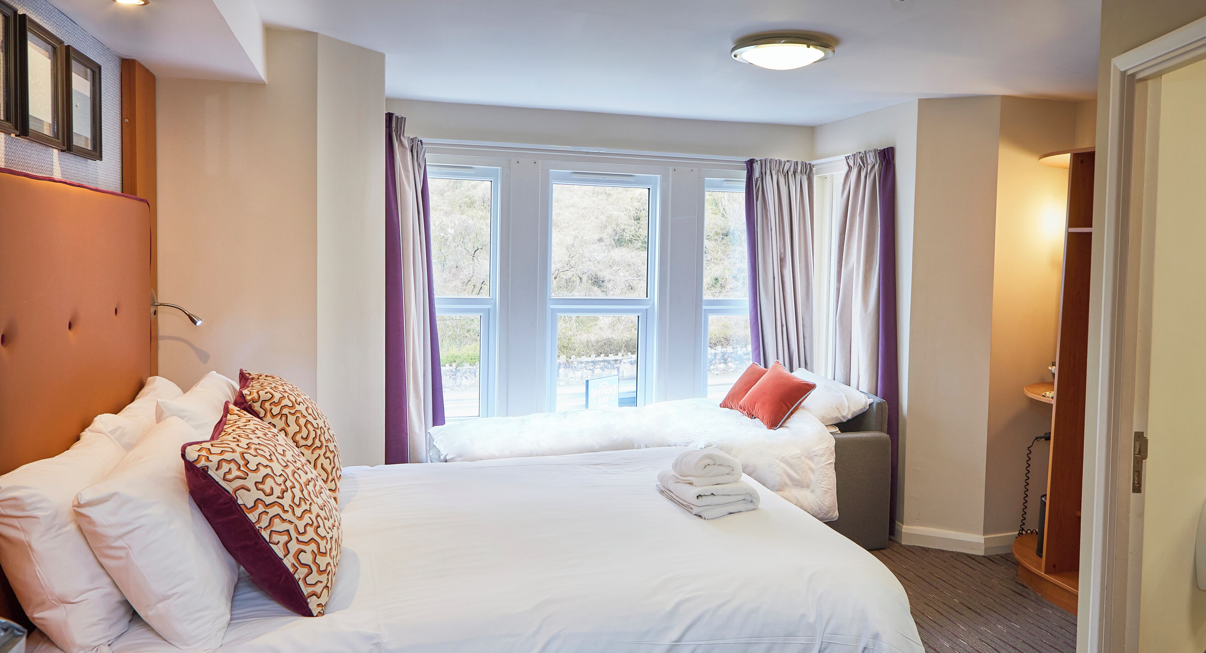 A hotel room with two beds, large windows, and a wooden floor.