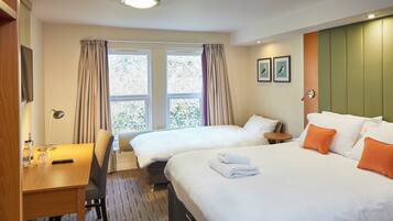 Une chambre d’hôtel avec deux lits, un bureau, une chaise, une petite table et une fenêtre avec des rideaux.