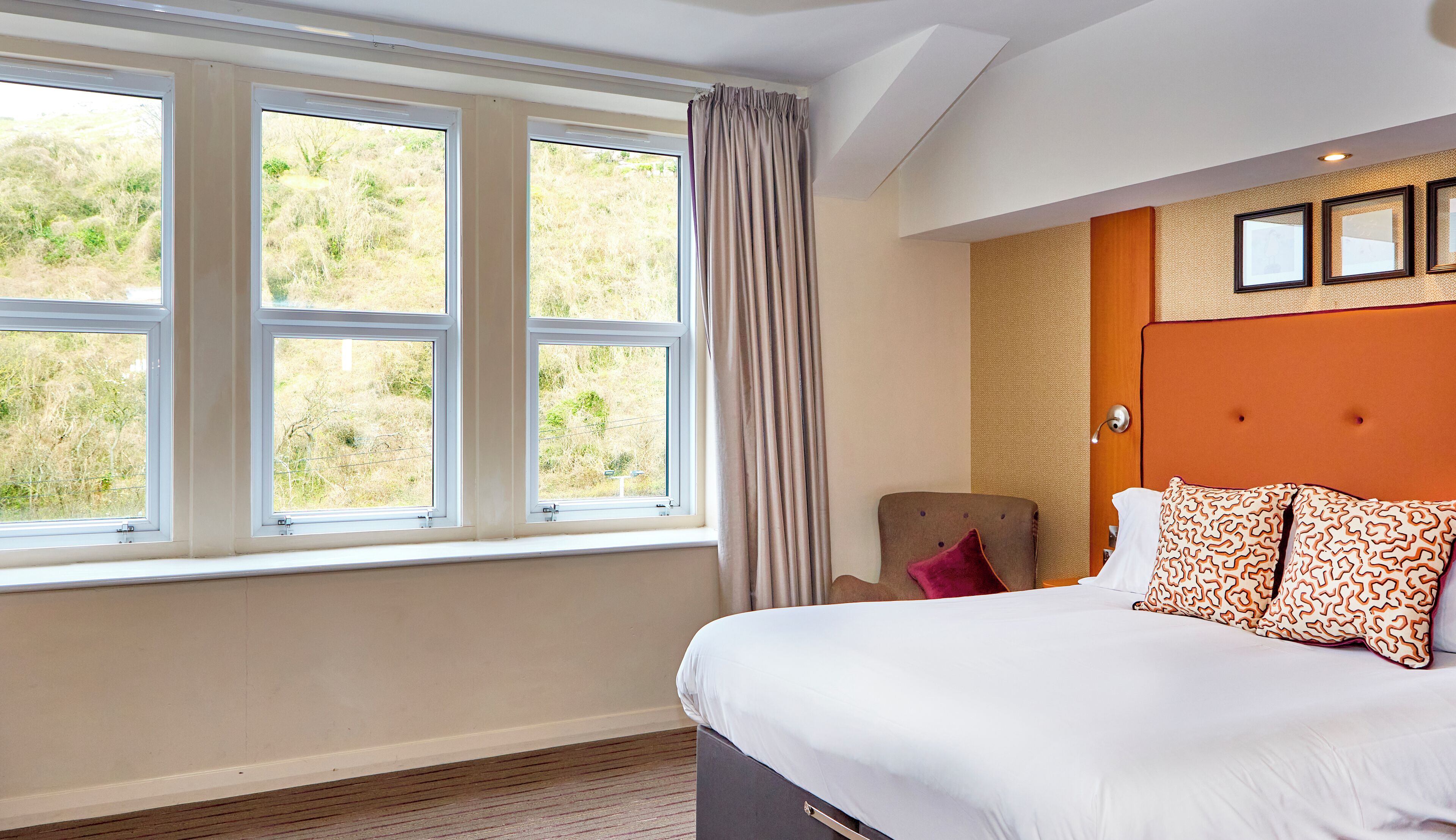 A hotel room with a large bed, a chair, and a window with curtains.