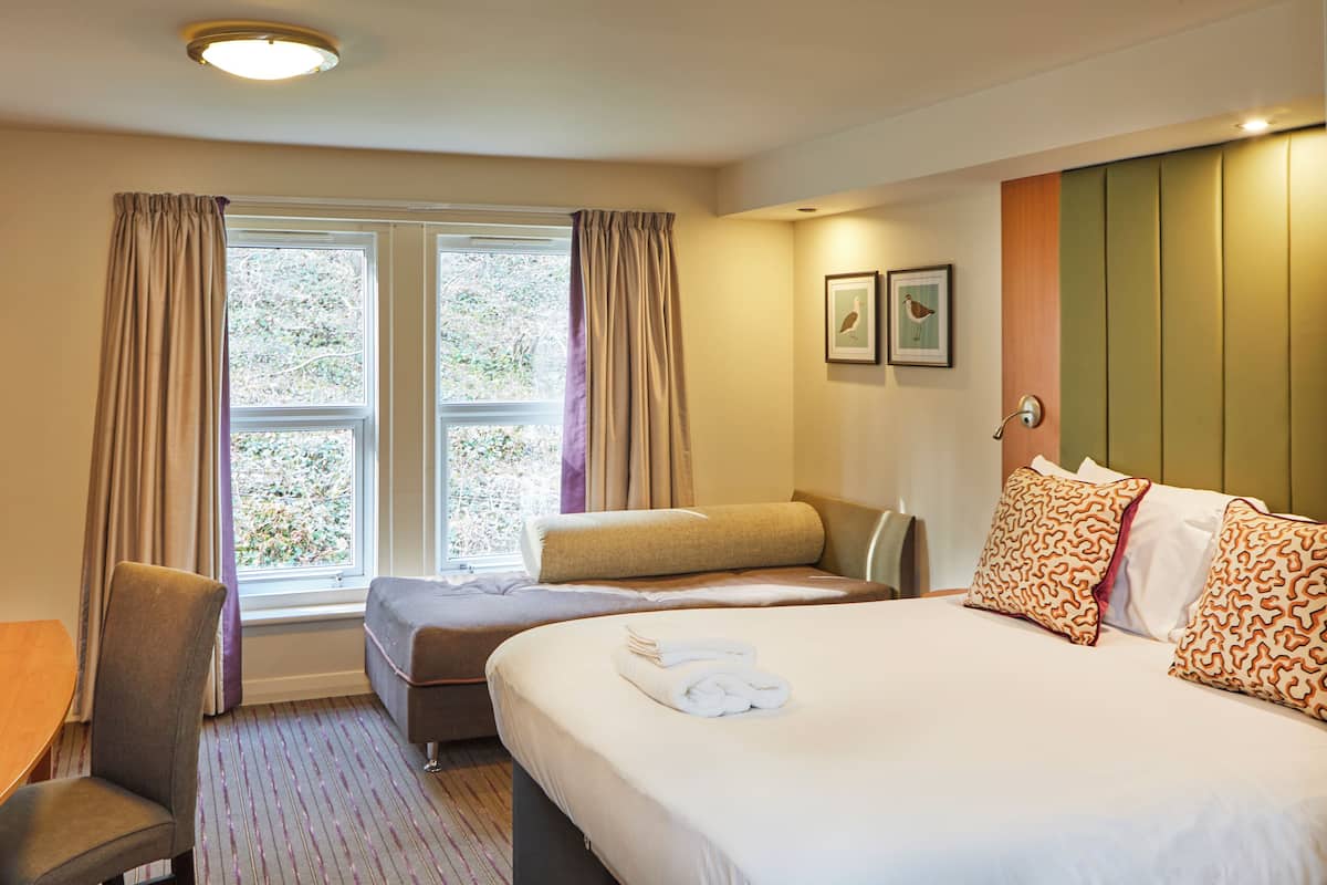 Une chambre d’hôtel avec un lit, un bureau, une chaise et une fenêtre avec des rideaux.