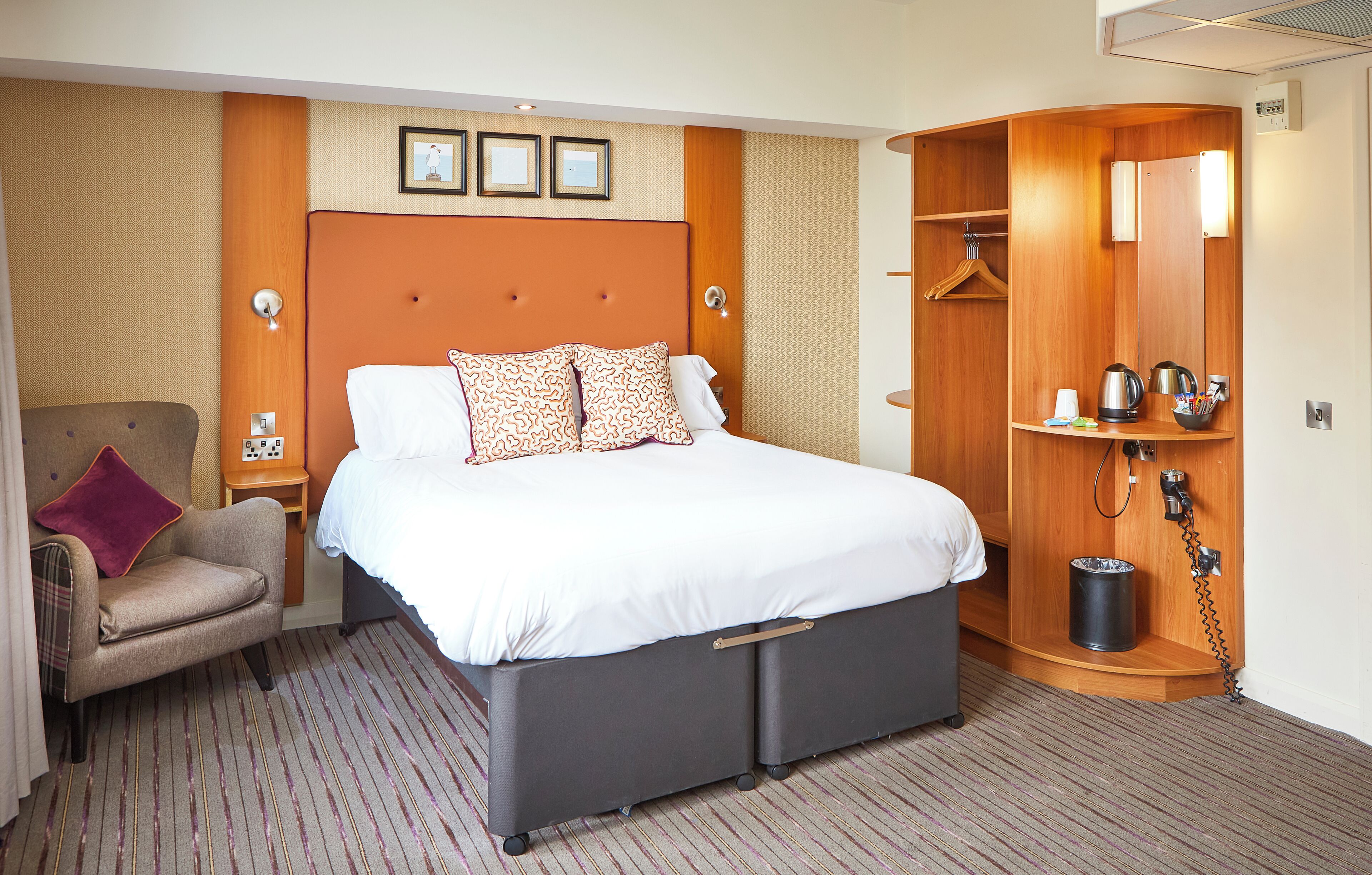 Hotelkamer met een groot bed, een stoel, een kledingkast en een tafeltje met waterkoker en kopjes.