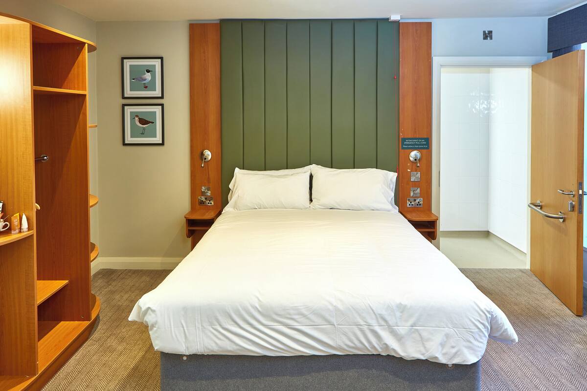 Une chambre d’hôtel avec un grand lit, une armoire en bois et deux tableaux encadrés au mur.