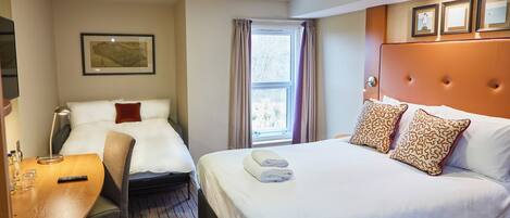 A hotel room with two beds, a desk, a chair, a window with curtains, and framed pictures on the wall.