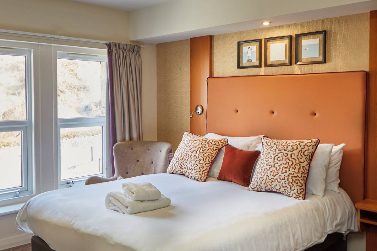 Une chambre d’hôtel avec un grand lit, une chaise, une table de chevet et une fenêtre avec des rideaux.