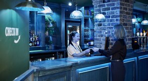 A bar area with a counter, shelves with bottles, and hanging lights.