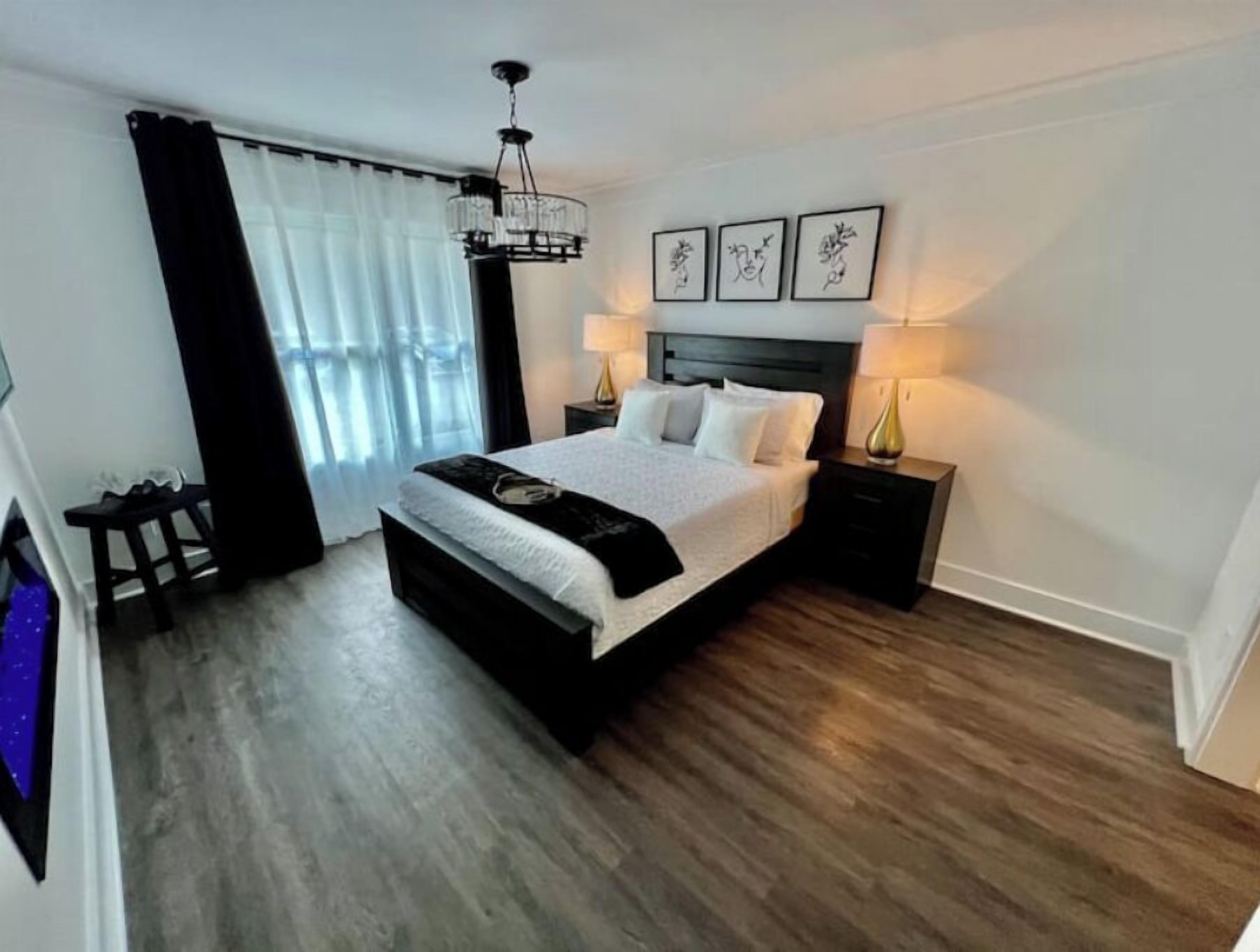 Un dormitorio moderno con una cama grande, mesitas de noche, una araña y obras de arte en la pared.