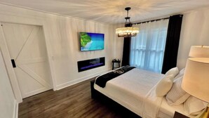 Een slaapkamer met een bed, een aan de muur bevestigde televisie, een kroonluchter en een raam met gordijnen.