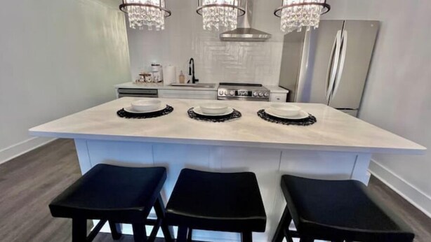 Een moderne keuken met een groot eiland, drie zwarte barkrukken en een roestvrijstalen koelkast.