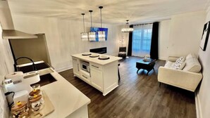 Een ruime woonkamer met een witte bank, een eettafel en een keuken met een wit kookeiland.