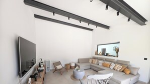 A modern living room with a large sectional sofa, a wooden coffee table, a rocking chair, and a flat-screen TV mounted on the wall. - La Bastide des Baux, Saint-Rémy-de-Provence, 6 CHB, 3 SDB, Salt pool 11x4,5 (Saint-Rémy-de-Provence)