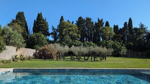 A swimming pool with a clear blue water surface, surrounded by a well-maintained lawn and a variety of trees and shrubs. - La Bastide des Baux, Saint-Rémy-de-Provence, 6 CHB, 3 SDB, Salt pool 11x4,5 (Saint-Rémy-de-Provence)