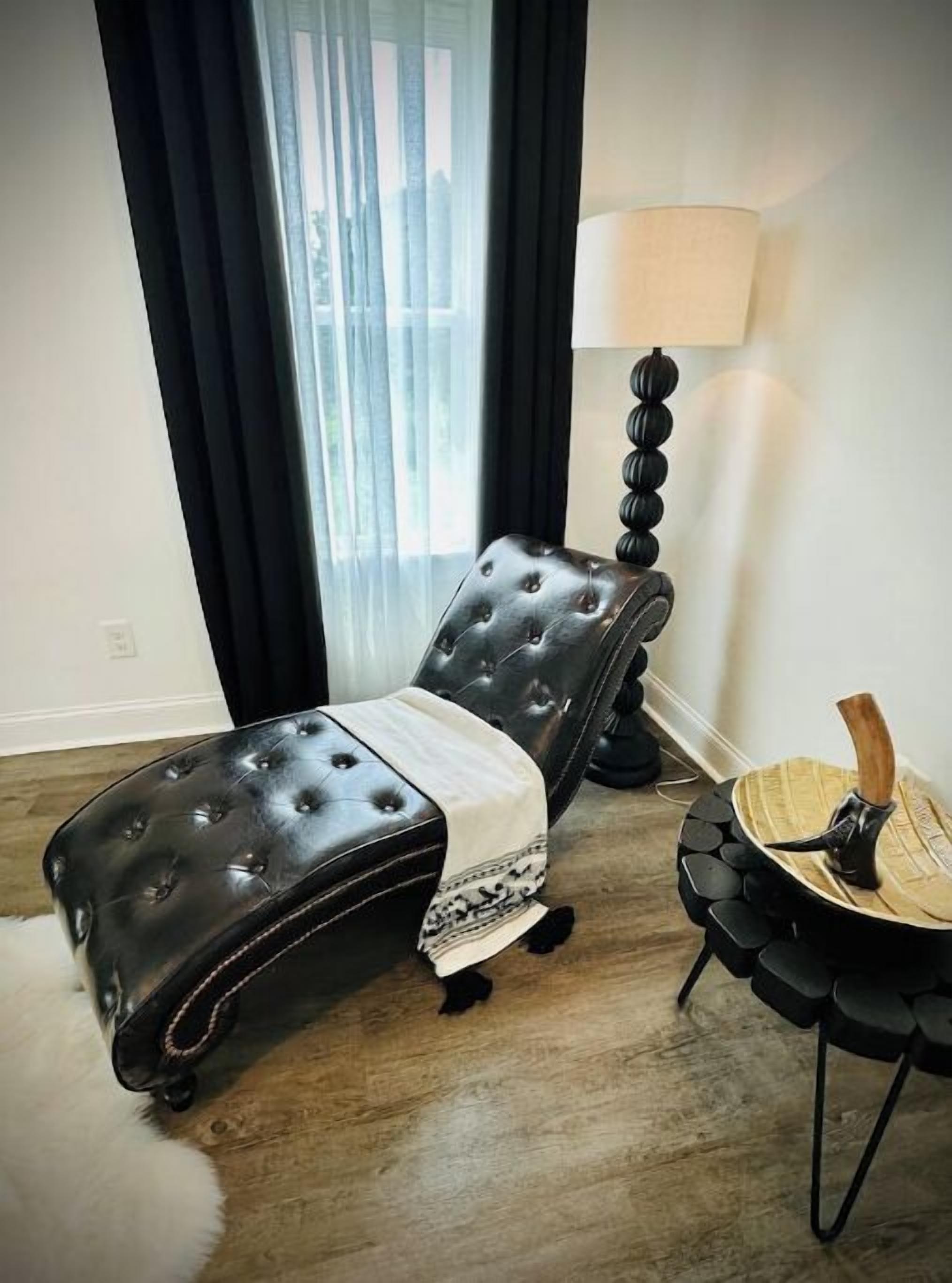 Quarto moderno com poltrona reclinável de couro preto, uma mesa redonda de madeira e um abajur.