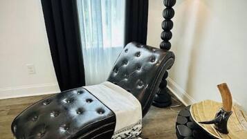 Quarto moderno com poltrona reclinável de couro preto, uma mesa redonda de madeira e um abajur.