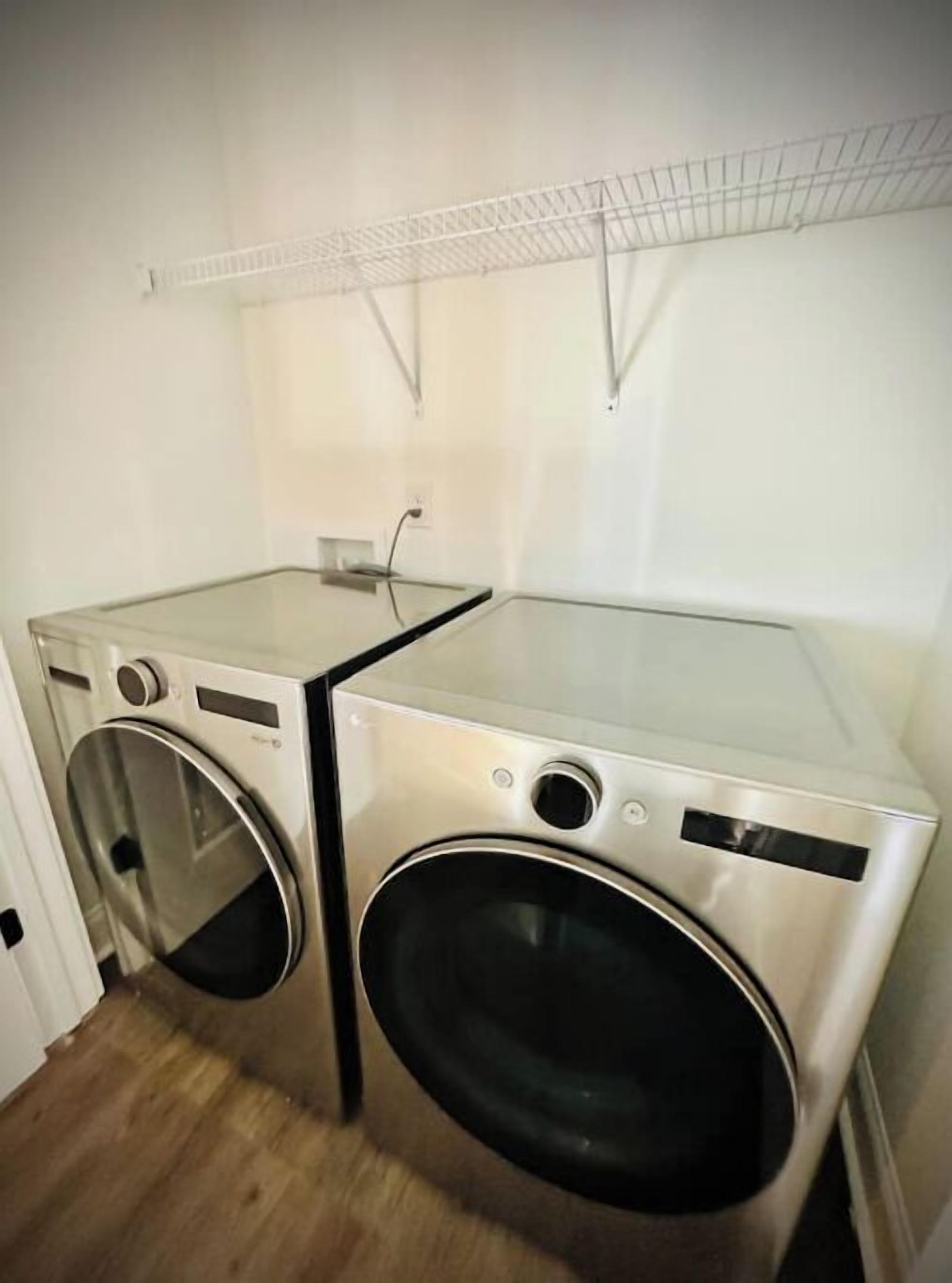 A compact laundry room with two stainless steel washing machines and a glass-top dryer.