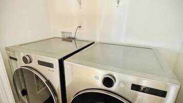A compact laundry room with two stainless steel washing machines and a glass-top dryer.