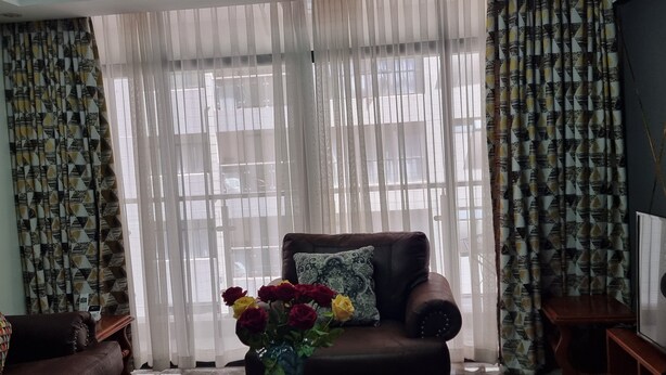 A living room with a brown sofa, a coffee table, and a vase with flowers. - Serenity Escape in Nairobi City (Nairobi)
