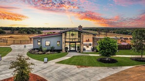 A modern house with a large glass front, a stone chimney, and a well-maintained lawn. - Longneck Manor (Fredericksburg)