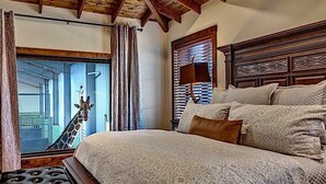 A bedroom with a large bed, a wooden headboard, a window with curtains, and a view of a giraffe outside. - Longneck Manor (Fredericksburg)