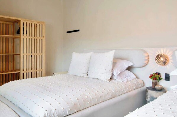 A bedroom with a bed, a wooden wardrobe, a bedside table with a vase of flowers, and a wall-mounted light fixture.