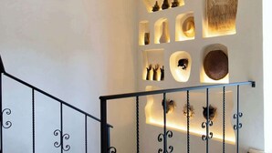 Una escala amb barana de metall negre, una paret blanca amb prestatgeries allà on hi ha diversos objectes decoratius, i un sostre de rajola.