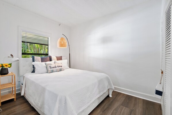 Une chambre à coucher avec un grand lit, une table de chevet avec une lampe et une fenêtre avec des stores.