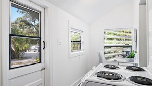 A kitchen with a white stove, a window with blinds, and a view of the street outside. - Charming 1-bed cottage in a Tropical Setting in West Palm Beach. Great location! (West Palm Beach)