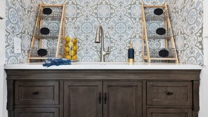 A bathroom with patterned wallpaper, a wooden vanity with a sink, and a towel rack. - Charming 1-bed cottage in a Tropical Setting in West Palm Beach. Great location! (West Palm Beach)