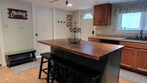 Una cocina con una isla central, taburetes de bar, armarios de madera, luces colgantes y un ventanal con vistas.