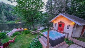 Una cabaña con jacuzzi, sillas de terraza y un muelle que se adentra en un lago.