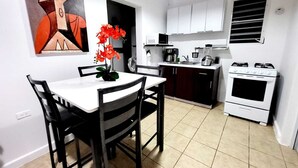 A compact kitchen with white cabinets, a stove, and a dining area with a table and chairs. - Casa Terruño, charming entire house with AC & Wi-Fi (Vega Baja)