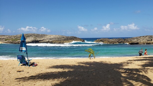 A beach with a blue umbrella, a chair, and a palm tree. - Casa Terruño, charming entire house with AC & Wi-Fi (Vega Baja)