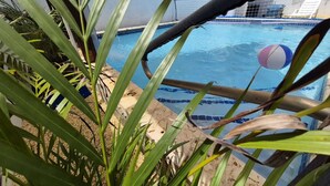 A pool with a blue tiled edge, surrounded by palm plants and a wooden deck. - Casa Terruño, charming entire house with AC & Wi-Fi (Vega Baja)