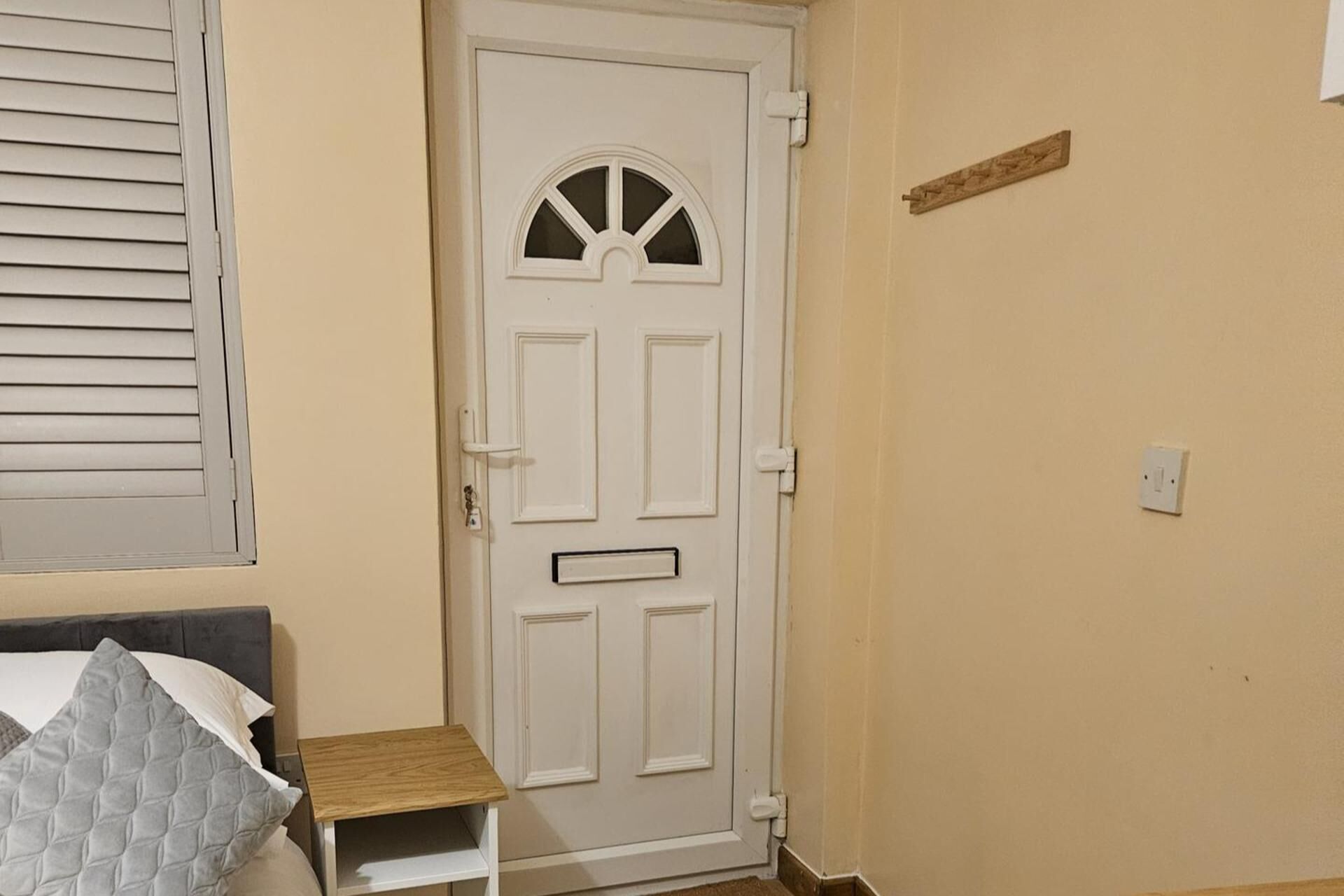 A room with a white door, a small wooden nightstand, and a bed with a grey quilt.