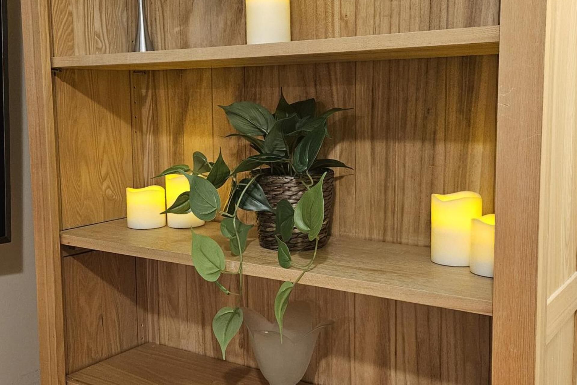 Una estantería de madera con plantas en macetas y velas.