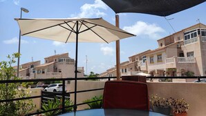 A balcony with a table and chair, a large umbrella, and a view of residential buildings. - La casa Divertido (VC)