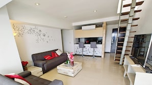 A modern living room with a sofa, a coffee table, and a TV. There is a kitchen area with a dining set and a staircase. - PENTHOUSE SPECTACULAR VIEW OF THE CITY (Guadalajara)