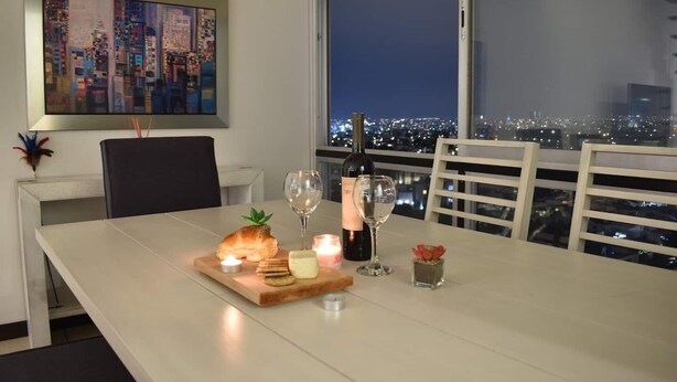 A dining table set with a croissant, candles, and wine glasses, overlooking a cityscape at night. - PENTHOUSE SPECTACULAR VIEW OF THE CITY (Guadalajara)