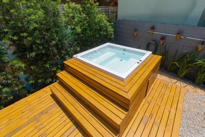 A hot tub on a wooden deck with a brick wall and potted plants in the background. - Pousada Hanalie - Praia do Rosa - SC (Imbituba)