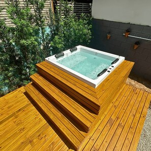 Een hottub op een houten terras, met een bakstenen muur en potplanten op de achtergrond.