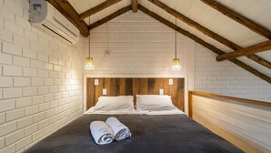 Habitació d'hotel amb parets de maó blanc, bigues de fusta, estriat de llit negre i dos tovalloles arremolinades sobre el llit.