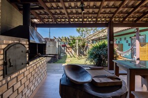 An outdoor patio with a brick oven, wooden table, and a hammock. - Pousada Hanalie - Praia do Rosa - SC (Imbituba)