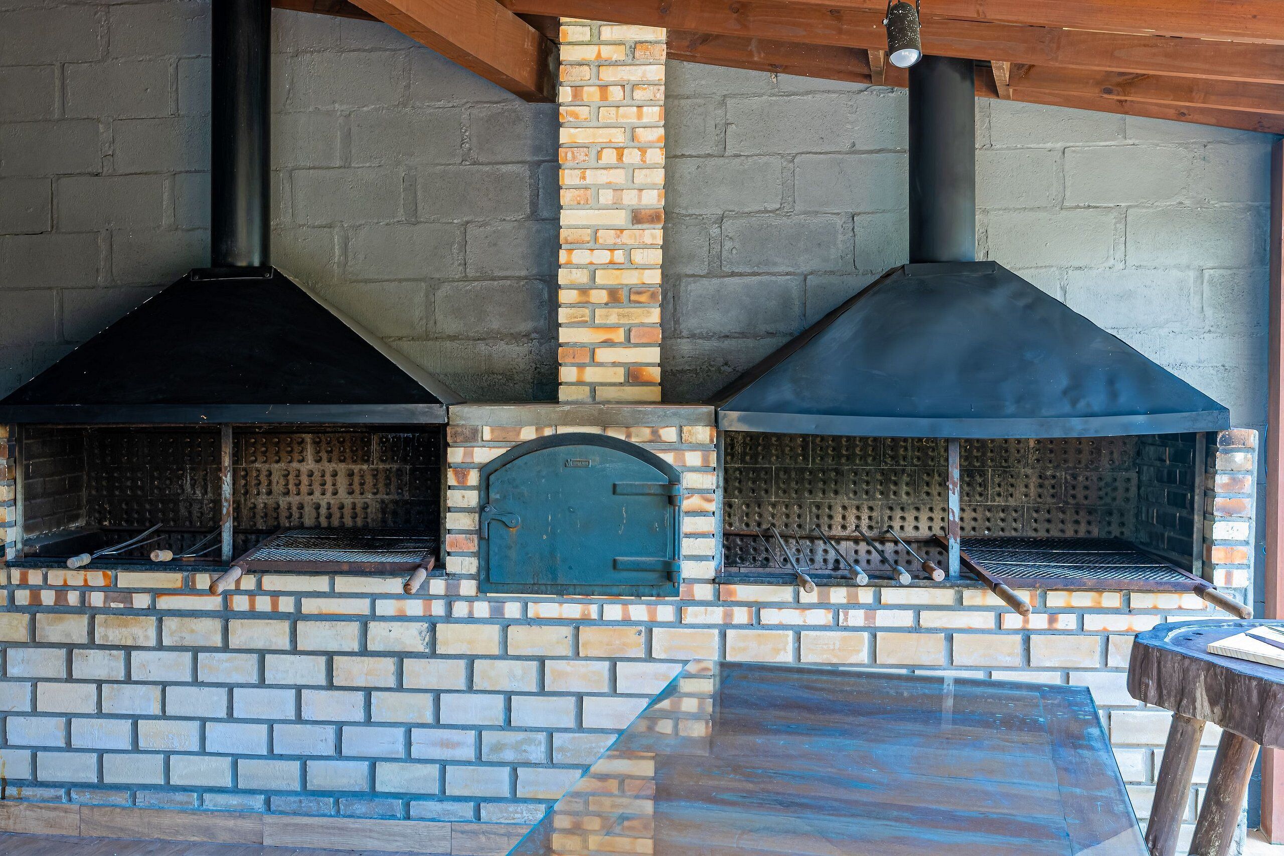 Un forno esterno in mattoni con canna fumaria, una porta in metallo e un tavolo anch'esso in metallo.