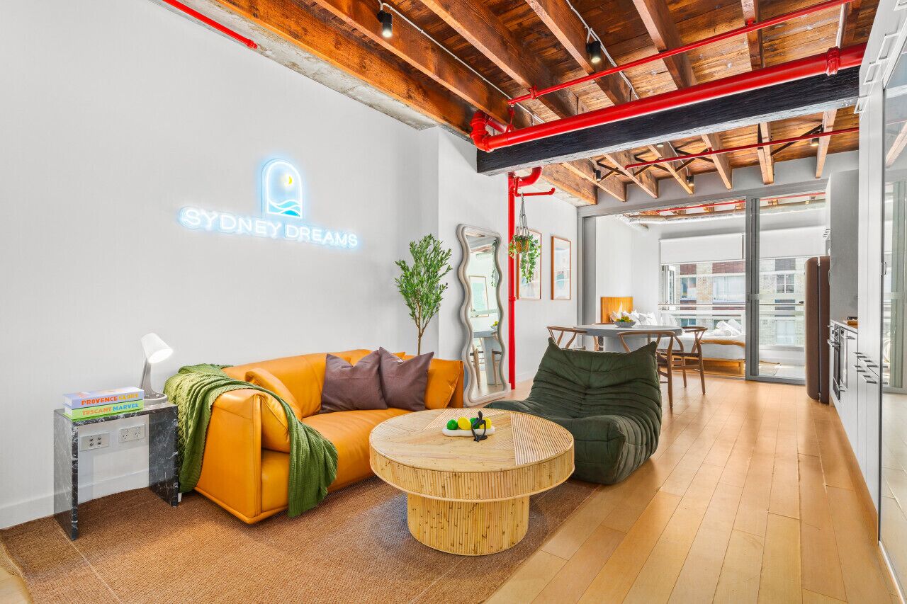 Ein modernes Wohnzimmer mit einer Couch, einem runden Couchtisch und einem Neon-Schild mit der Aufschrift 'SYDNEY DREAMS'.