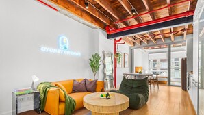 Un salon moderne avec un canapé, une table basse ronde et un panneau lumineux au néon sur lequel on peut lire « SYDNEY DREAMS ».