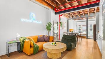 Ein modernes Wohnzimmer mit einer Couch, einem runden Couchtisch und einem Neon-Schild mit der Aufschrift 'SYDNEY DREAMS'.
