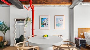 Un coin repas avec une table ronde, quatre chaises et un saladier de fruits. Deux œuvres d’art encadrées ornent le mur, ainsi qu’une pipe rouge et un plafond en bois.