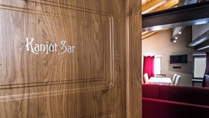 Eine Holztür mit der Aufschrift "Kapljot Bar", die zu einem Raum führt, in dem sich ein rotes Sofa und ein Esstisch befinden.