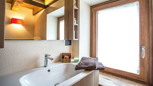 Ein Badezimmer mit einem großen Spiegel, einem weißen Waschbecken, einem Holzschrank und einem Fenster mit Tür.